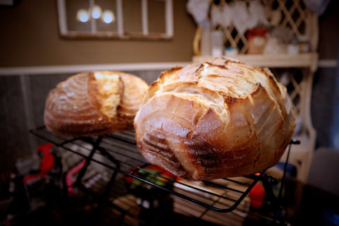 Two freshly baked sourdough bread loaves on a black cooling rack in a kitchen setting.