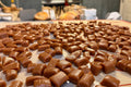 A large assortment of glossy brown candies or caramels spread out on baking mats on a table in a home kitchen setting.